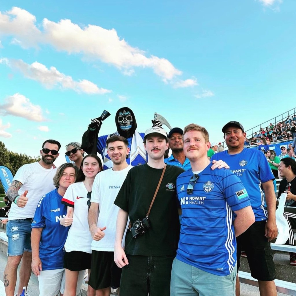 A group of Charlotte Independence fans at a game at Paladin Stadium. They are standing with the bleachers behind them.