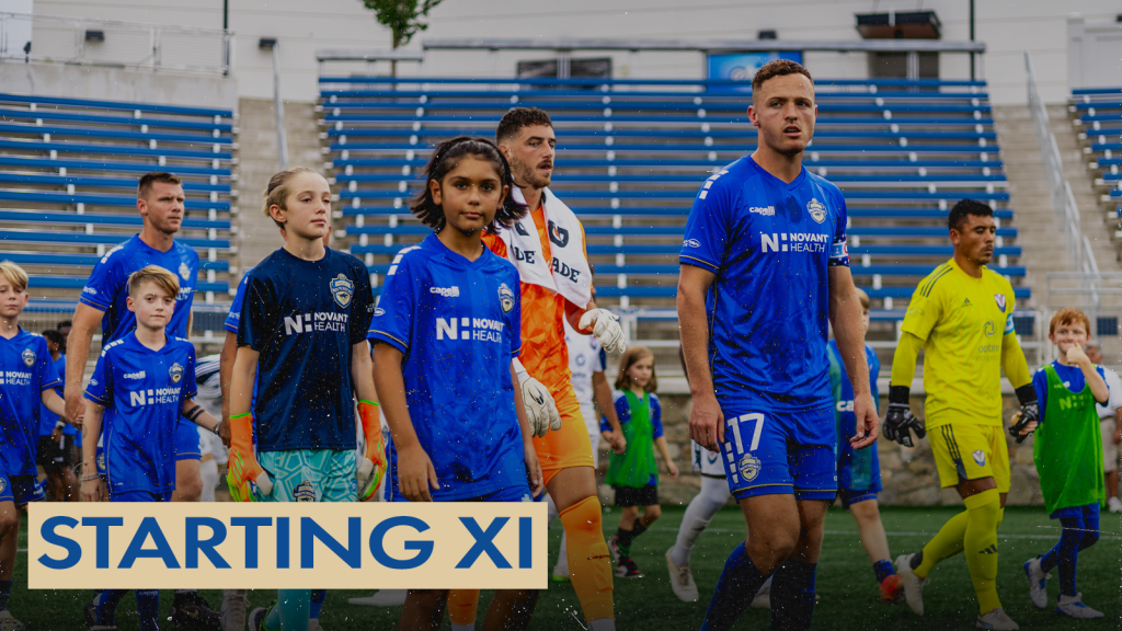 A photo of the Charlotte Independence and South Georgia Tormenta starting lineups walking onto the field at American Legion Memorial Stadium for the national anthem. There are kids wearing Charlotte Independence jerseys walking with the professional players. There is a gold text box in the bottom left corner with blue text that says "Starting XI".